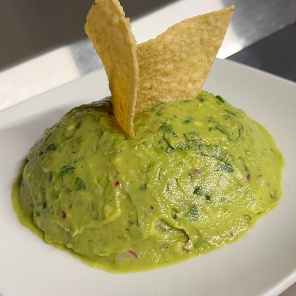 A mound of vibrant green guacamole with two golden tortilla chips on a white plate.