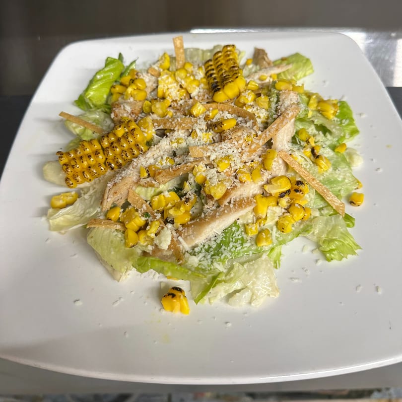 A vibrant salad with grilled corn, shredded chicken, tortilla strips, and grated cheese on a white plate.