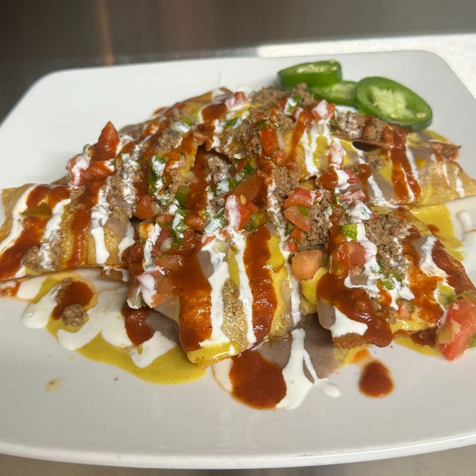 A plate of beef enchiladas topped with red sauce, sour cream, pico de gallo, and jalapeños.